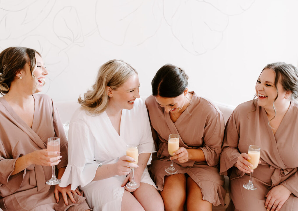 A group of girls getting ready for a wedding day, bridesmaids with the bride, laughing and having cocktails
